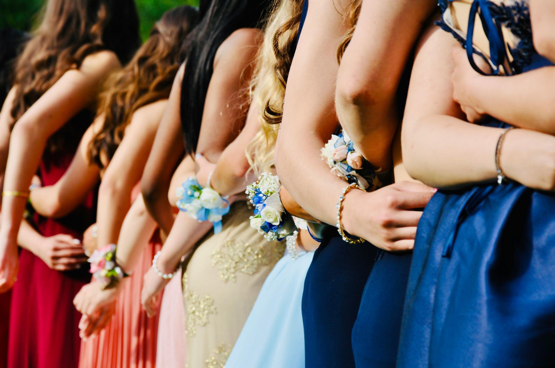 A group of students in prom dresses stand with their backs to the camera