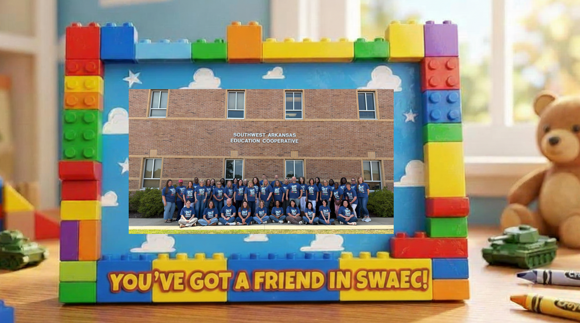 **Alt text (WCAG 2.1 AA compliant):**  Group photo of approximately 30 staff members wearing black SWAEC shirts, posing outside a brick building with a sign reading “Southwest Arkansas Education Cooperative.” Some are standing and others are seated on the grass in front of the building.