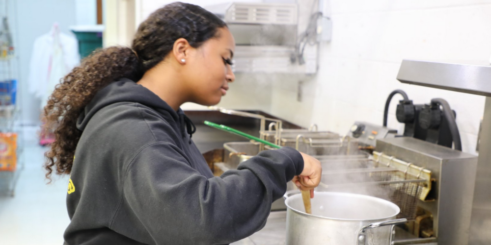 student stirring pot of food