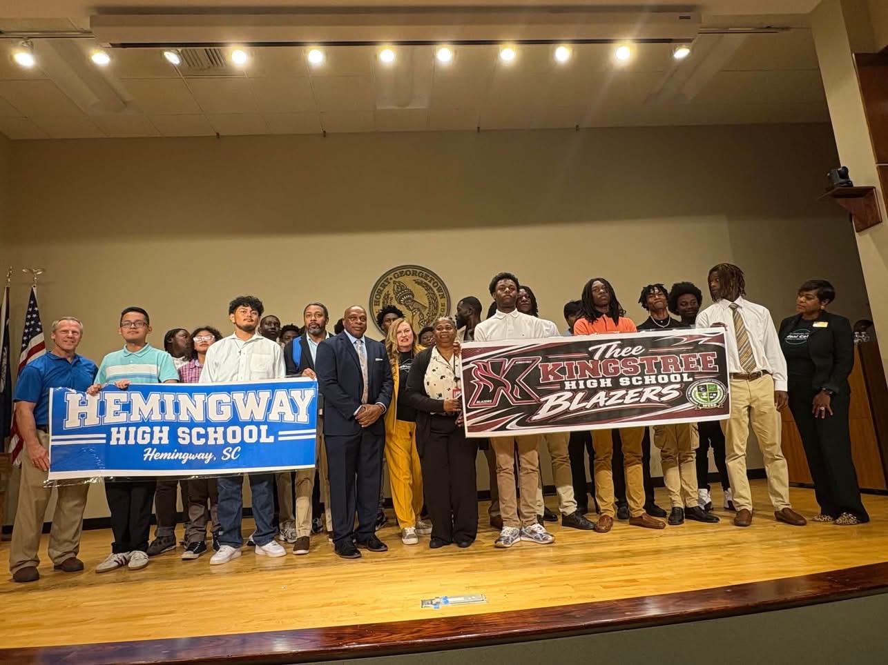 Students and adults pose on a stage holding banners for Hemingway High School and the Kingstree High School Blazers.