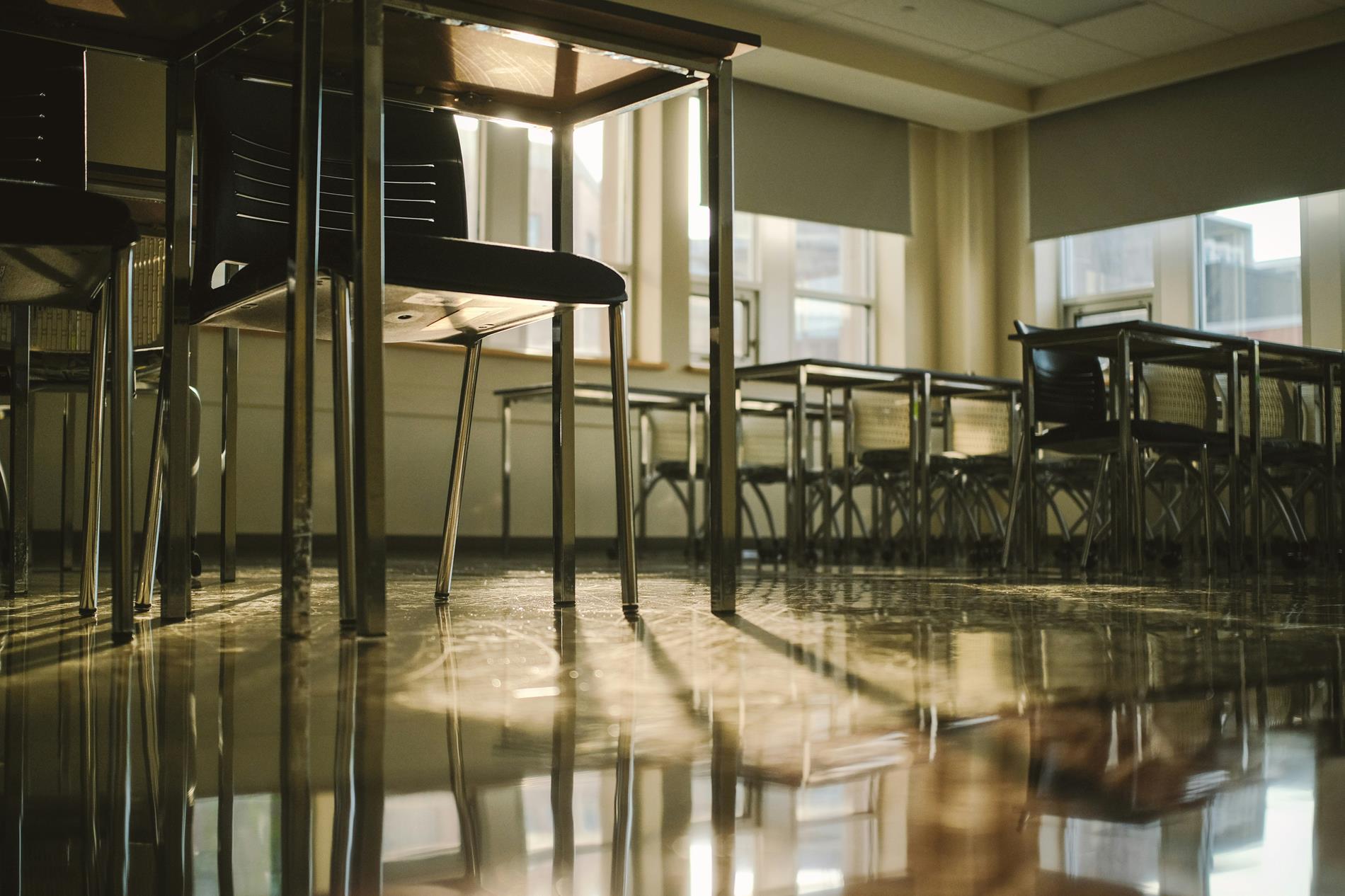 A series of empty desks sit in a classroom in late afternoon light