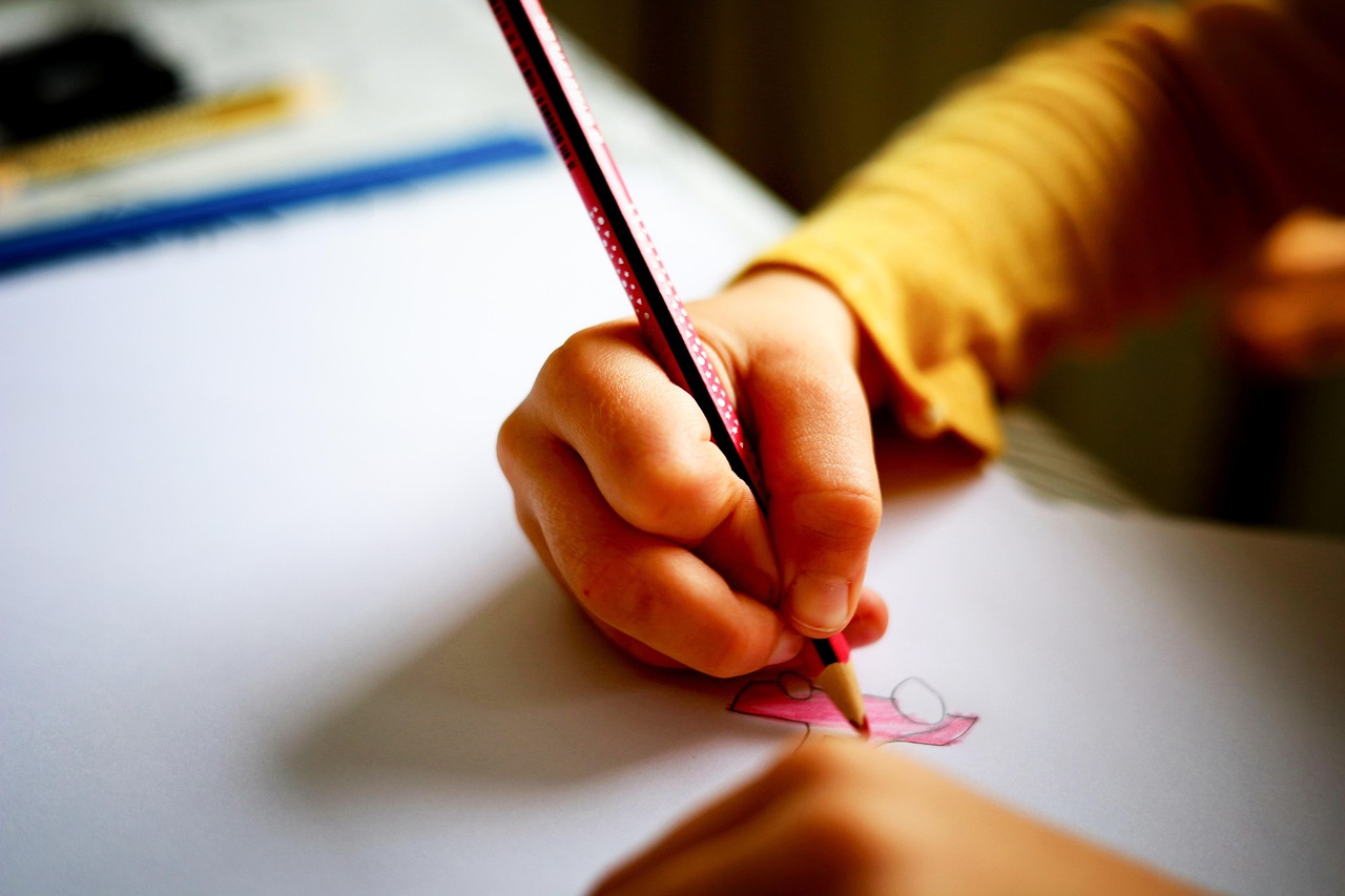 A young student draws on a piece of paper with a pencil