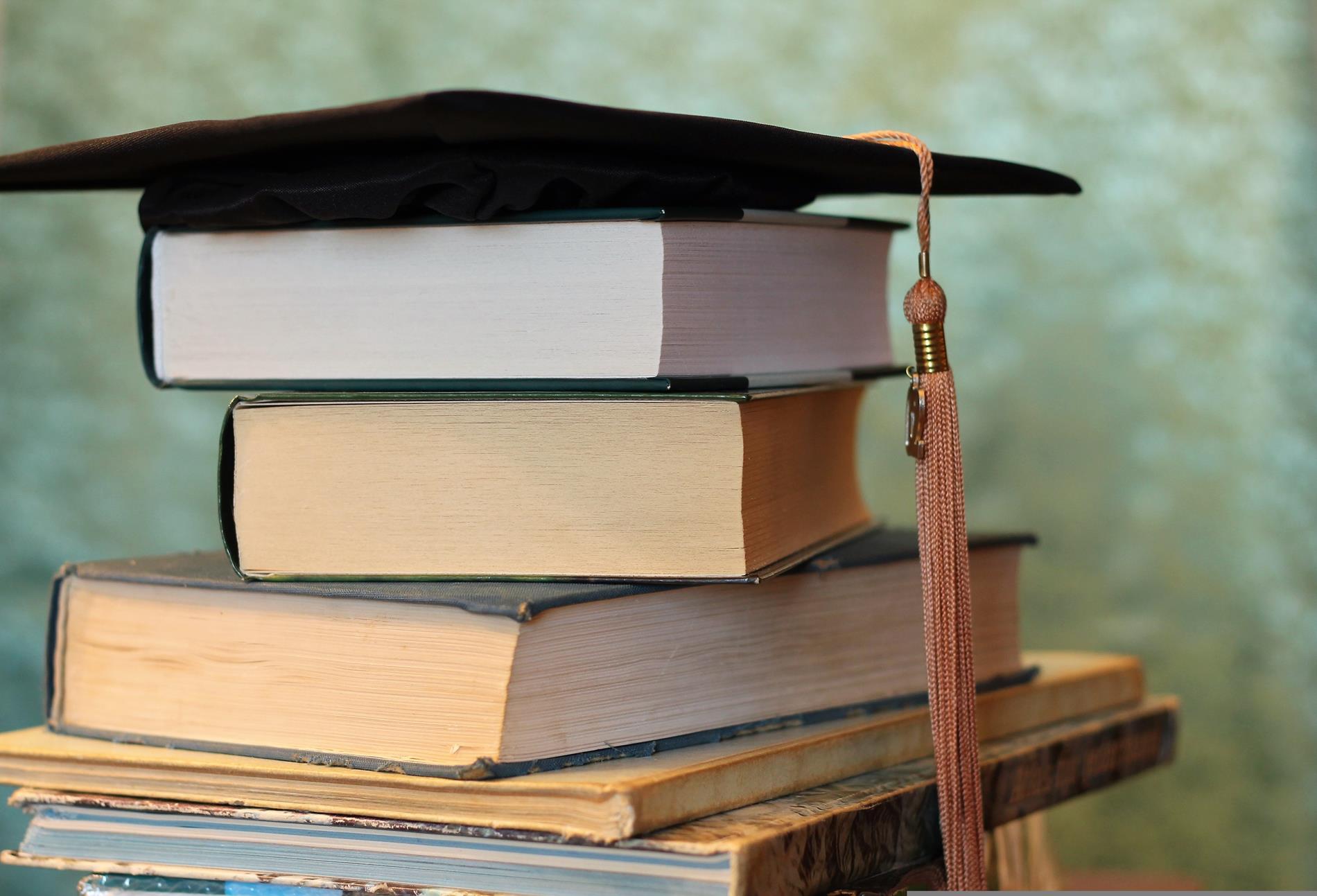 An image of books stacked with a graduation cap on top