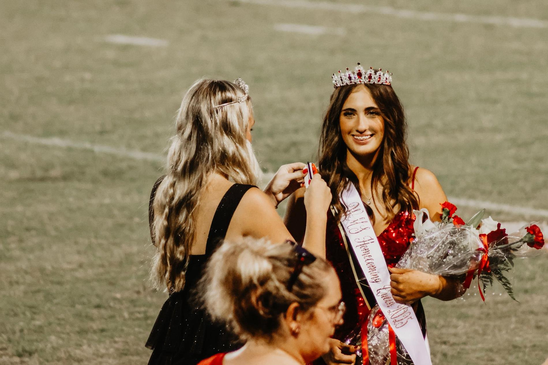 Crowned homecoming queen in a red dress with bouquet.