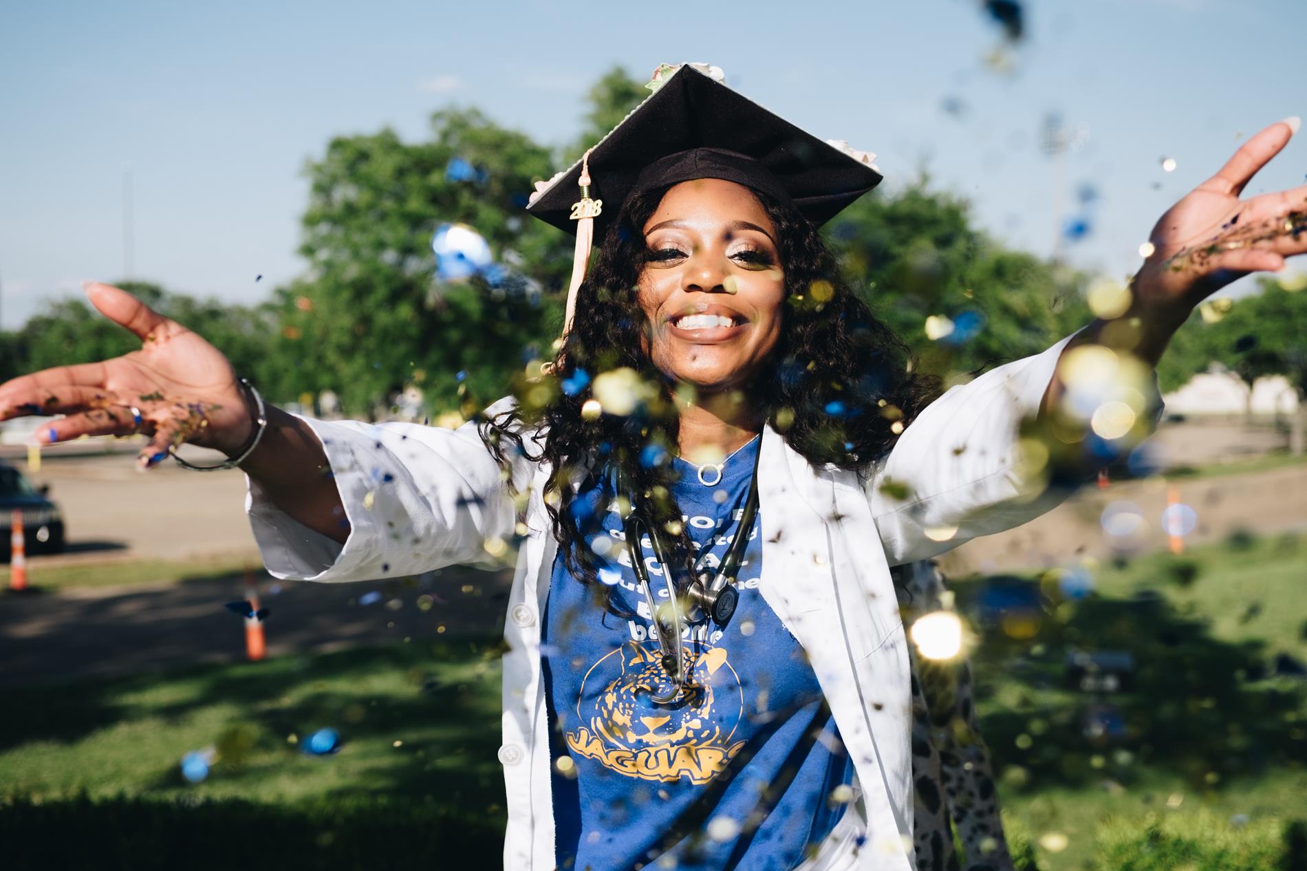 a young woman throws confetti while wearing a black graduation robe and cap