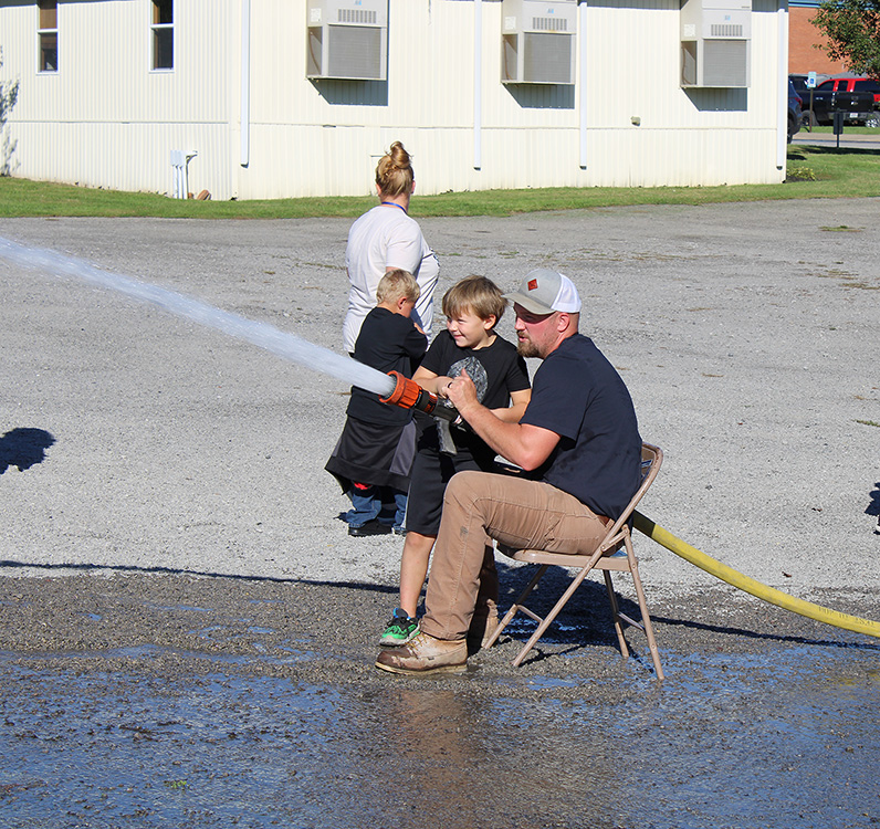 Fire Fighter Andrew Russell helps students with the fire hose