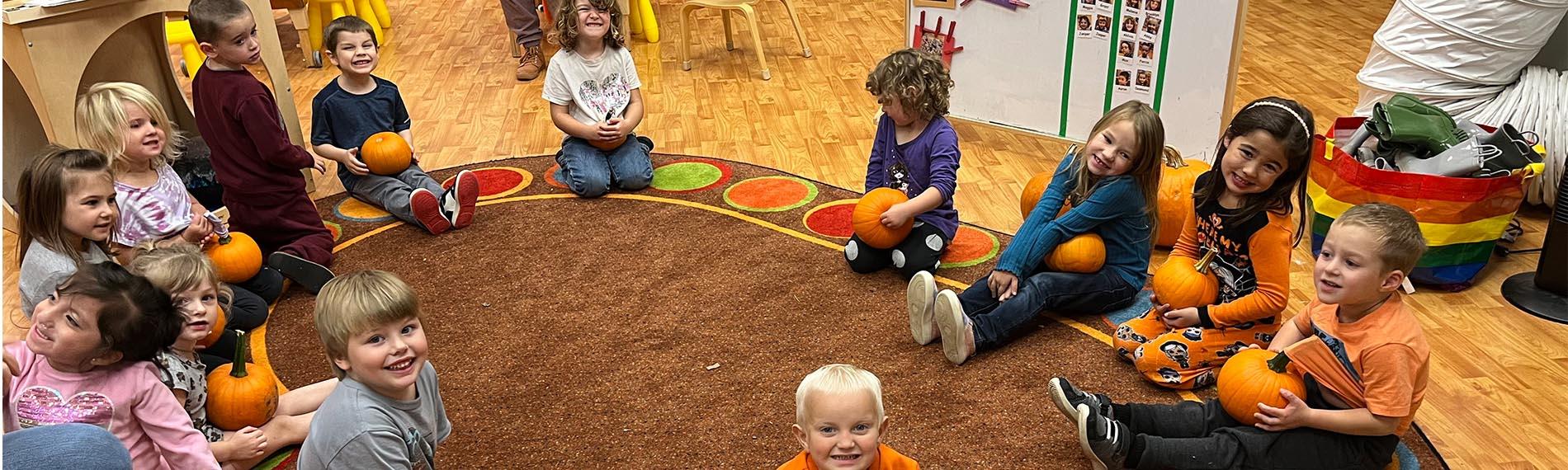 Preschool students sitting on the circle carpet with their pumpkins