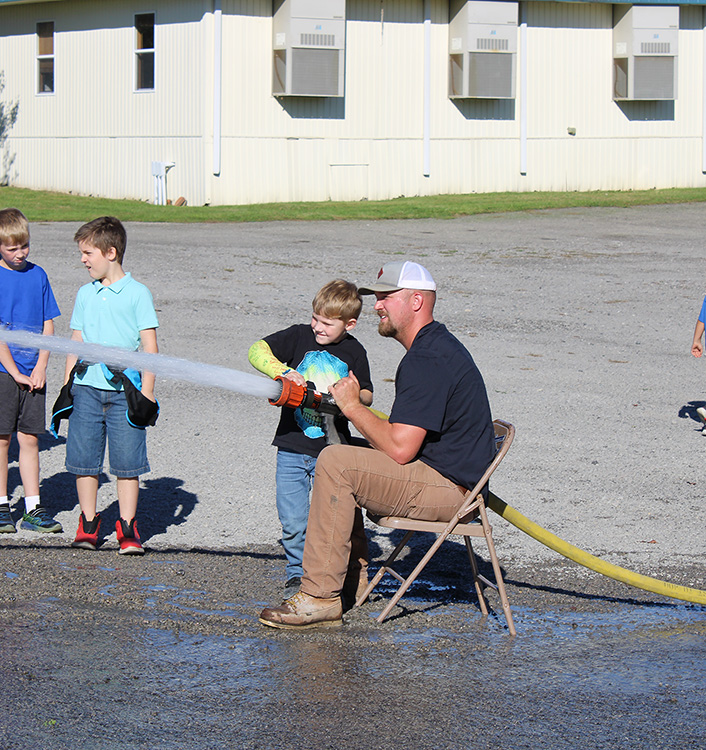 Fire Fighter Andrew Russell helps students with the fire hose