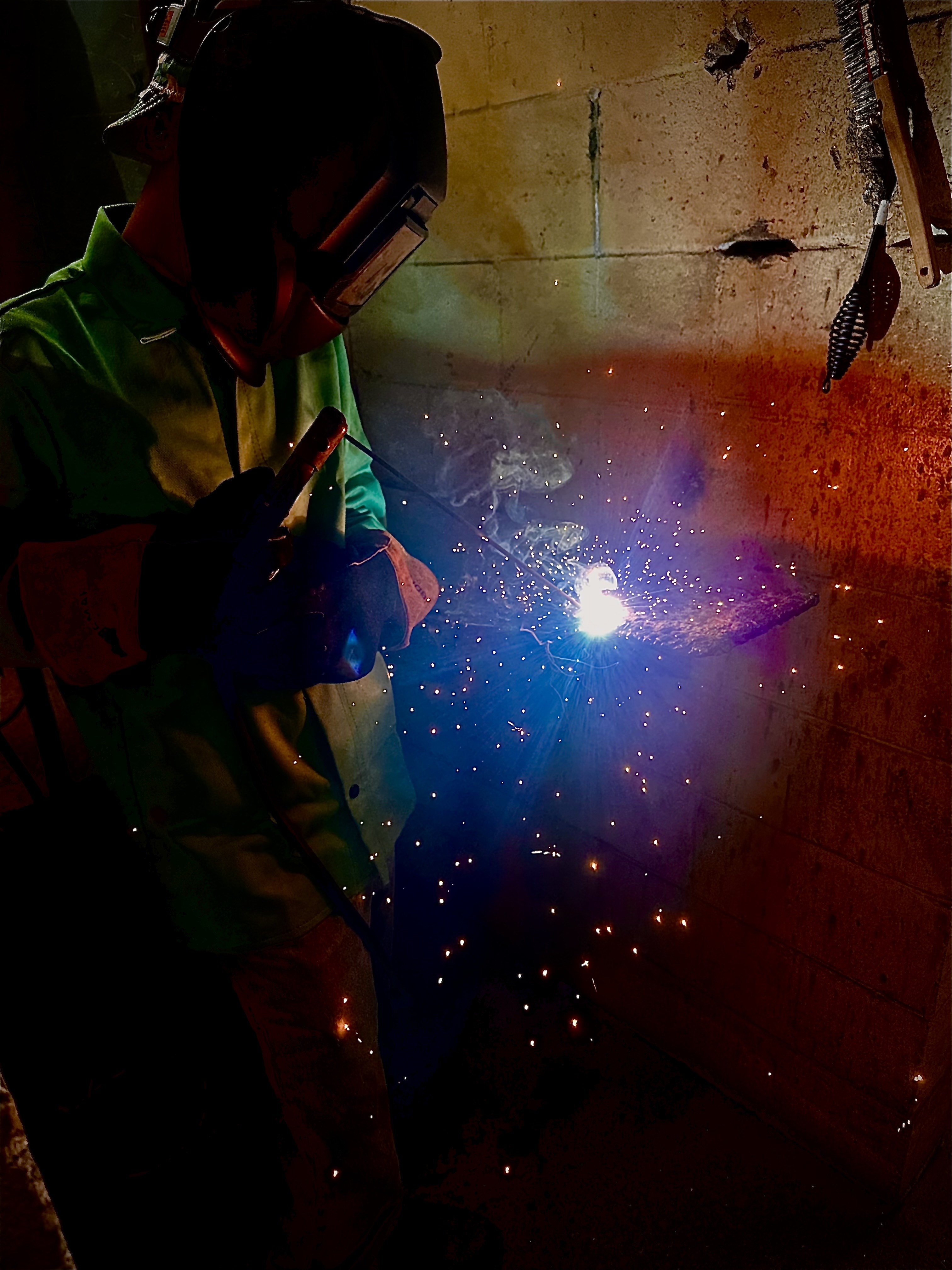 Student using a welding machine with hood on and arc showing.