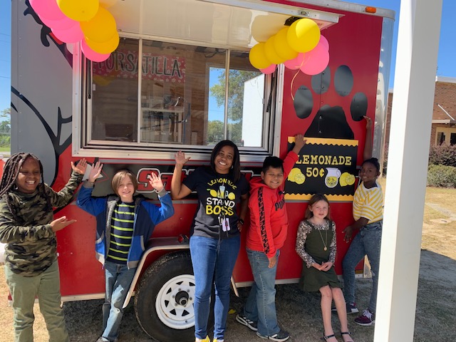 Teacher and students in front of lemonade stand