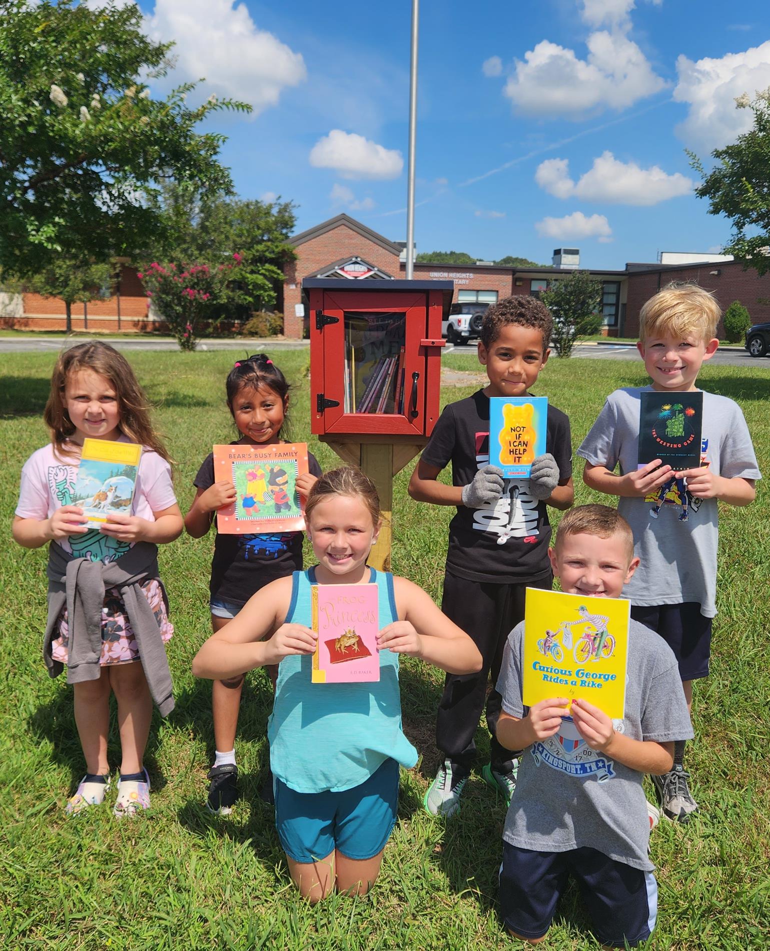 Photo of students holding books in front of the Little Free Library
