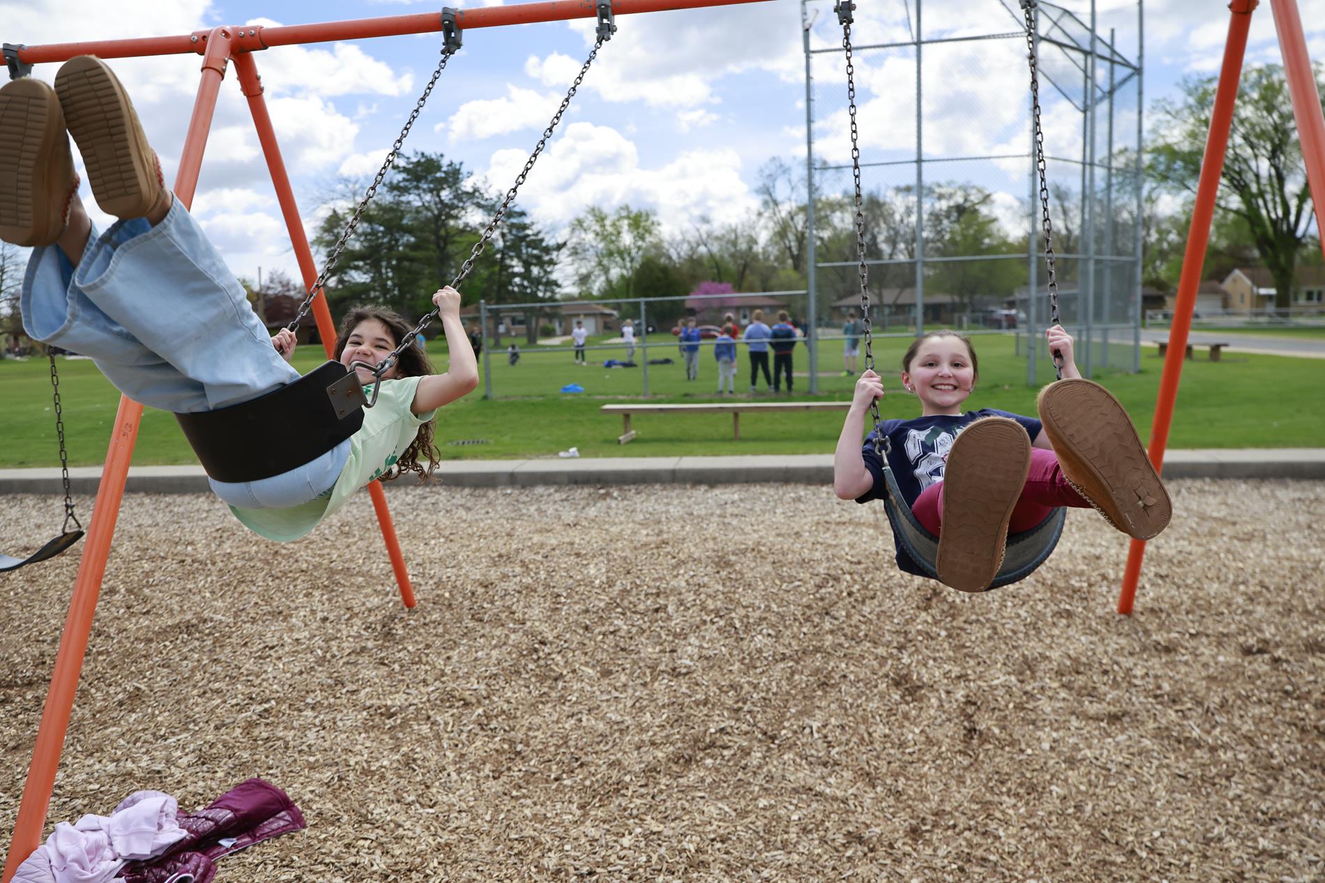 Two students smiling while swinging on swing set on playground