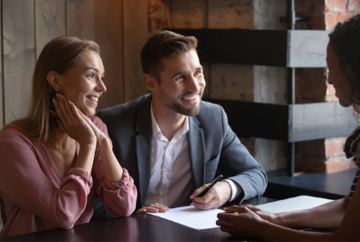 a smiling man and woman sitting across the table from an interviewer