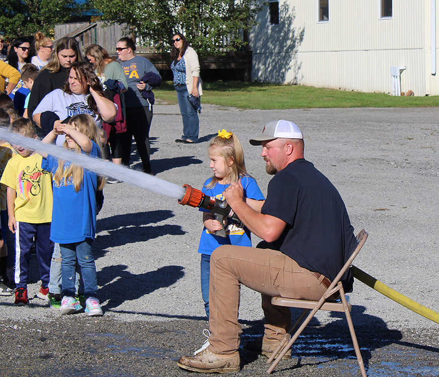 Fire Fighter Andrew Russell helps students with the fire hose