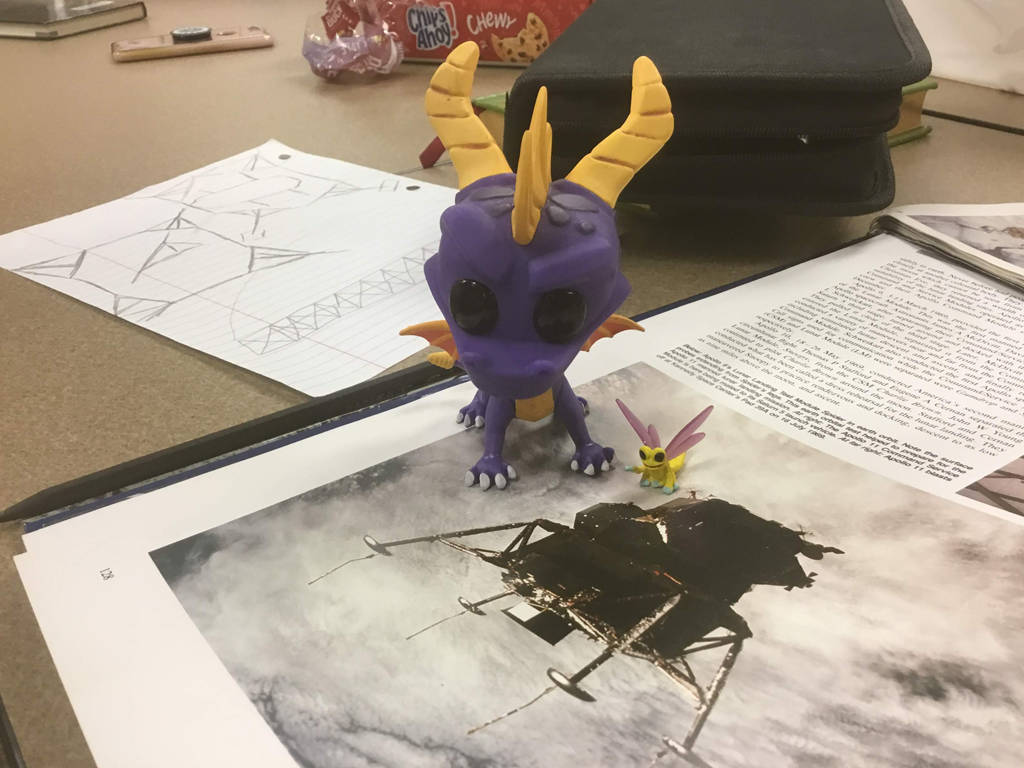 toy figure of a dragon placed on a book lying on table open to a photograph of the Apollo 11 Lunar Module