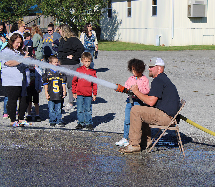 Fire Fighter Andrew Russell helps students with the fire hose