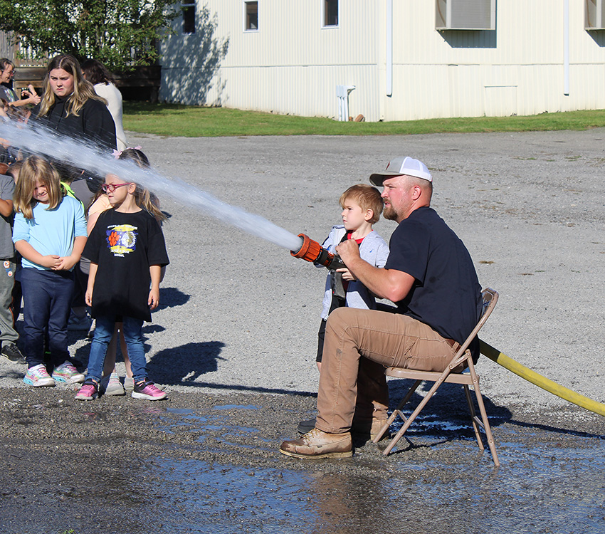 Fire Fighter Andrew Russell helps students with the fire hose