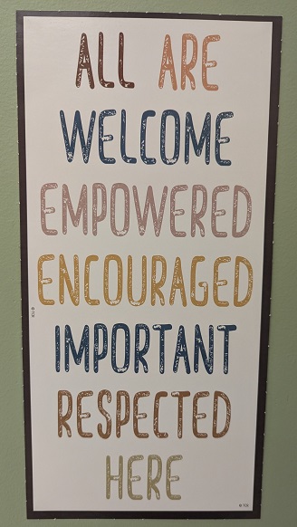 Image of a sign. Sign reads "All are welcome empowered encouraged important respected here"