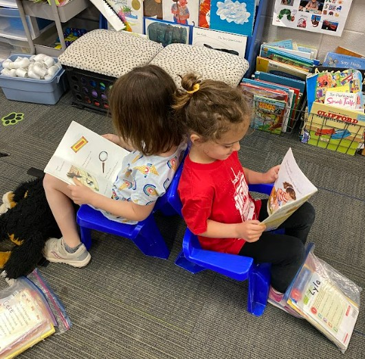 Two young girls at Central Park Elementary sit back to back in small chairs while reading books
