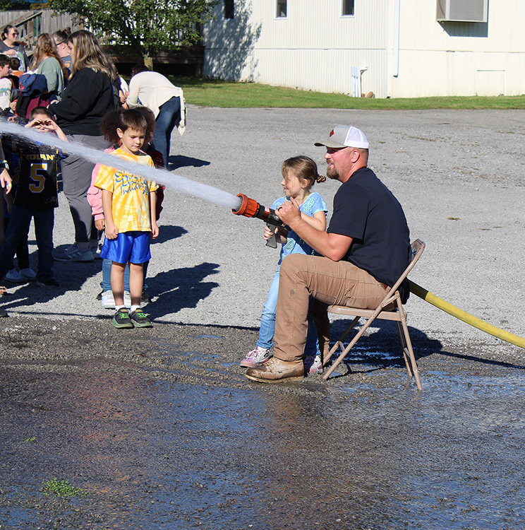 Fire Fighter Andrew Russell helps students with the fire hose