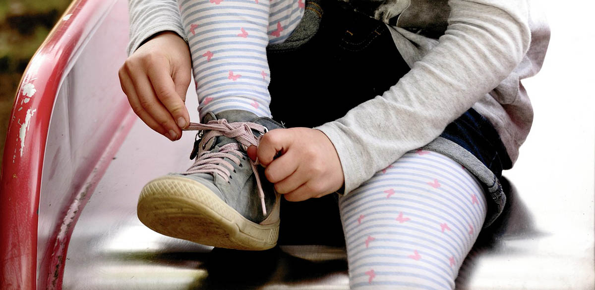 A young girl sits on a metal slide tying her shoe