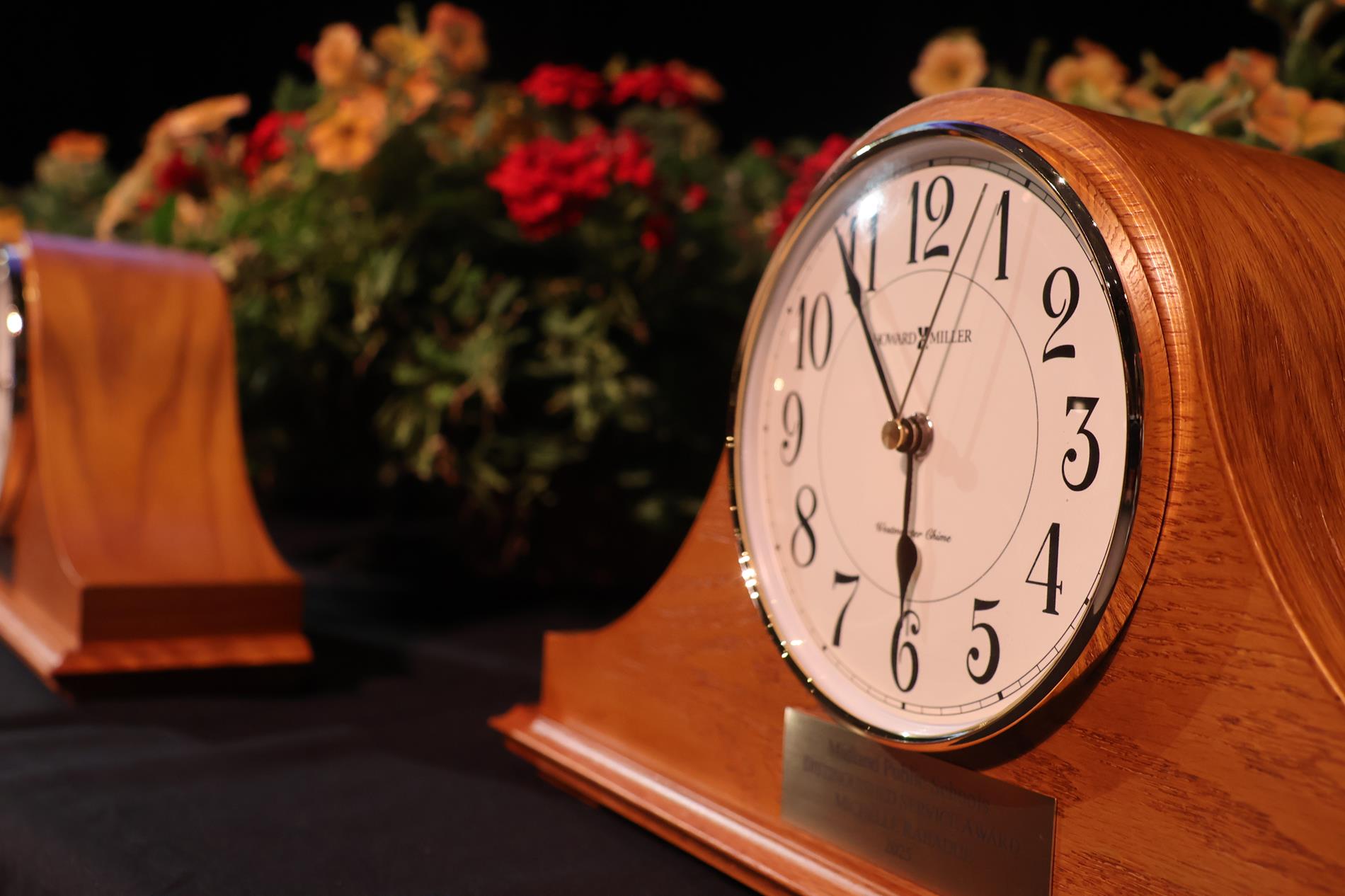A clock award sits on a table in front of flowers
