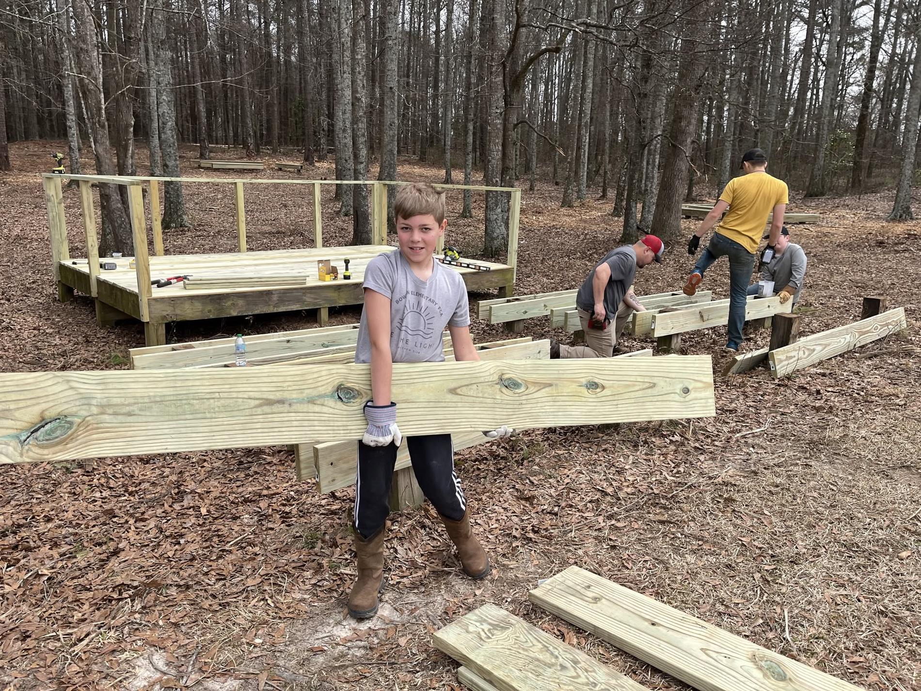 BMS student, Gunner Parlier, holding wood assisting in the rebuilding of the outdoor classroom