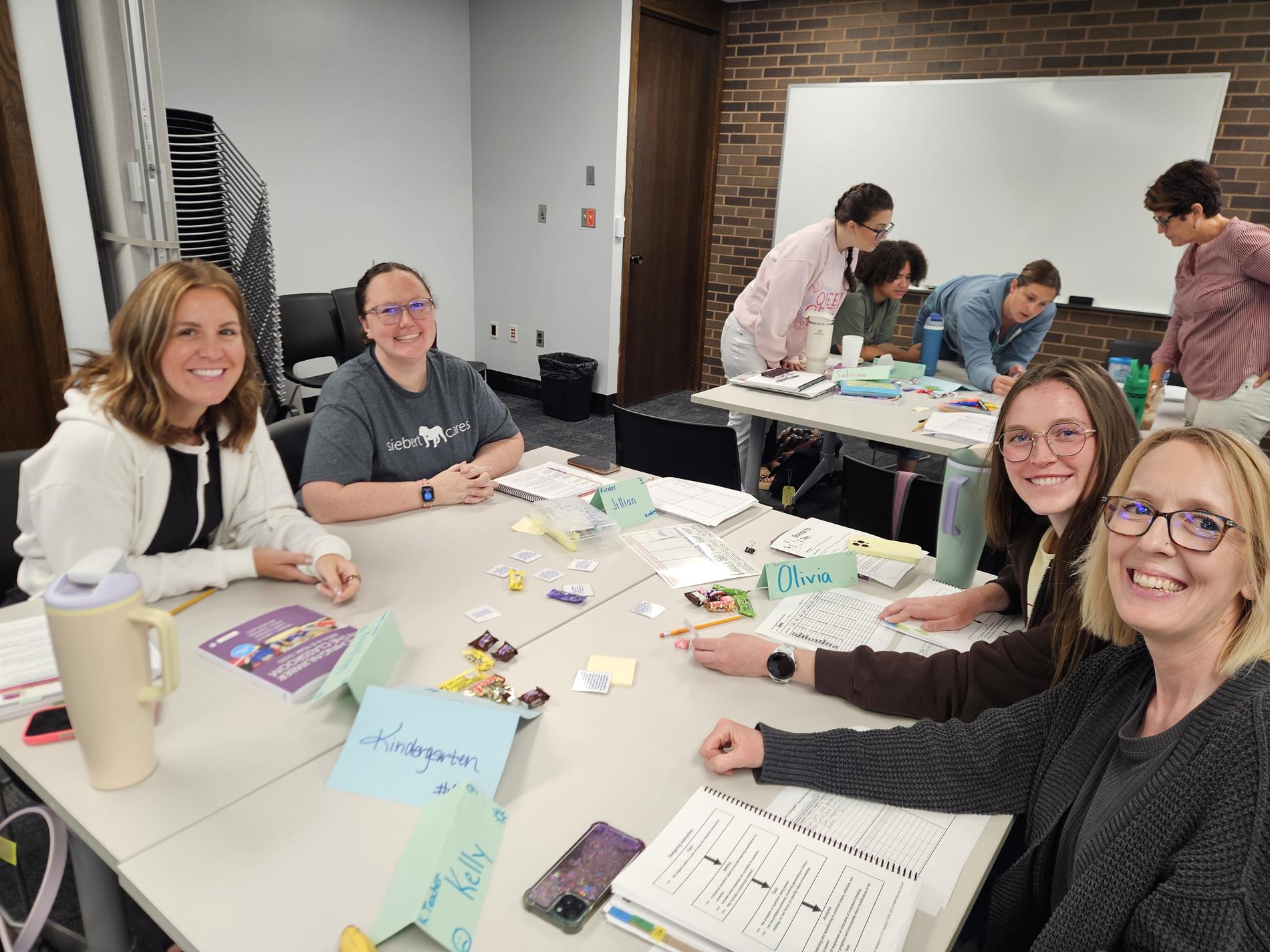 A group of female teachers sit and smile at the camera while sitting at desks during professional development
