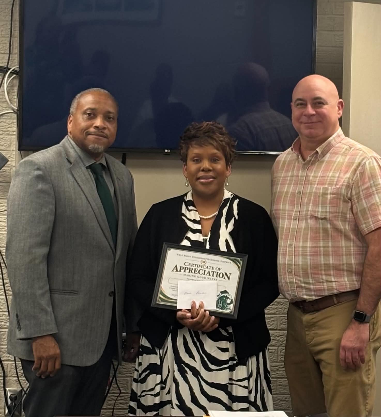 Superintendent Dr. Jermaine Taylor and Learning Center Principal Richard Bryant standing with Administrative Assistant Monica Pippins as she holds her Making Good Waves certificate of appreciation.
