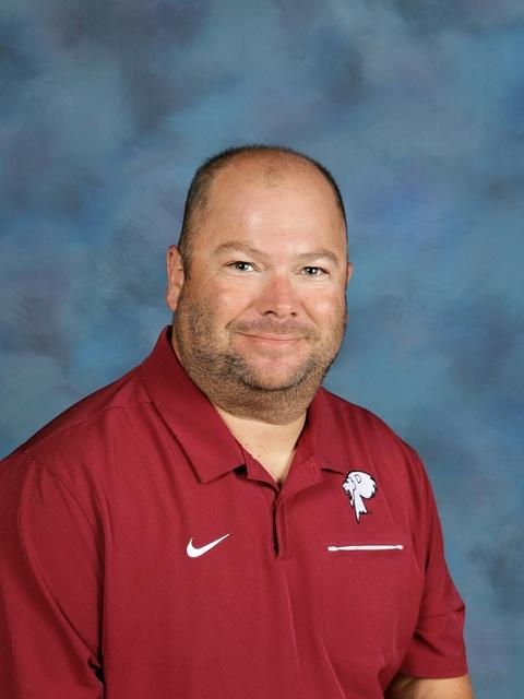 Coach Riddle sitting, smiling, in a cardinal polo