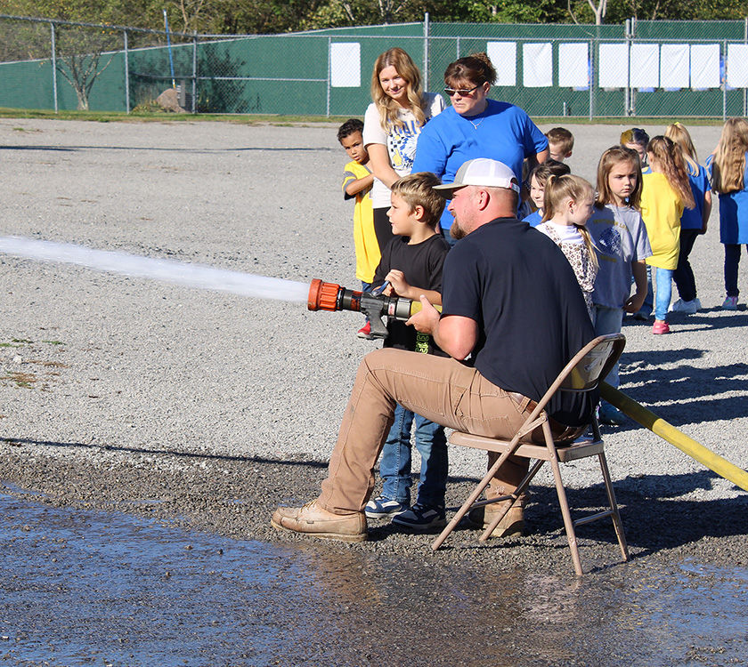 Fire Fighter Andrew Russell helps students with the fire hose