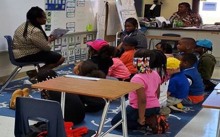 teacher reading to students sitting on the floor 