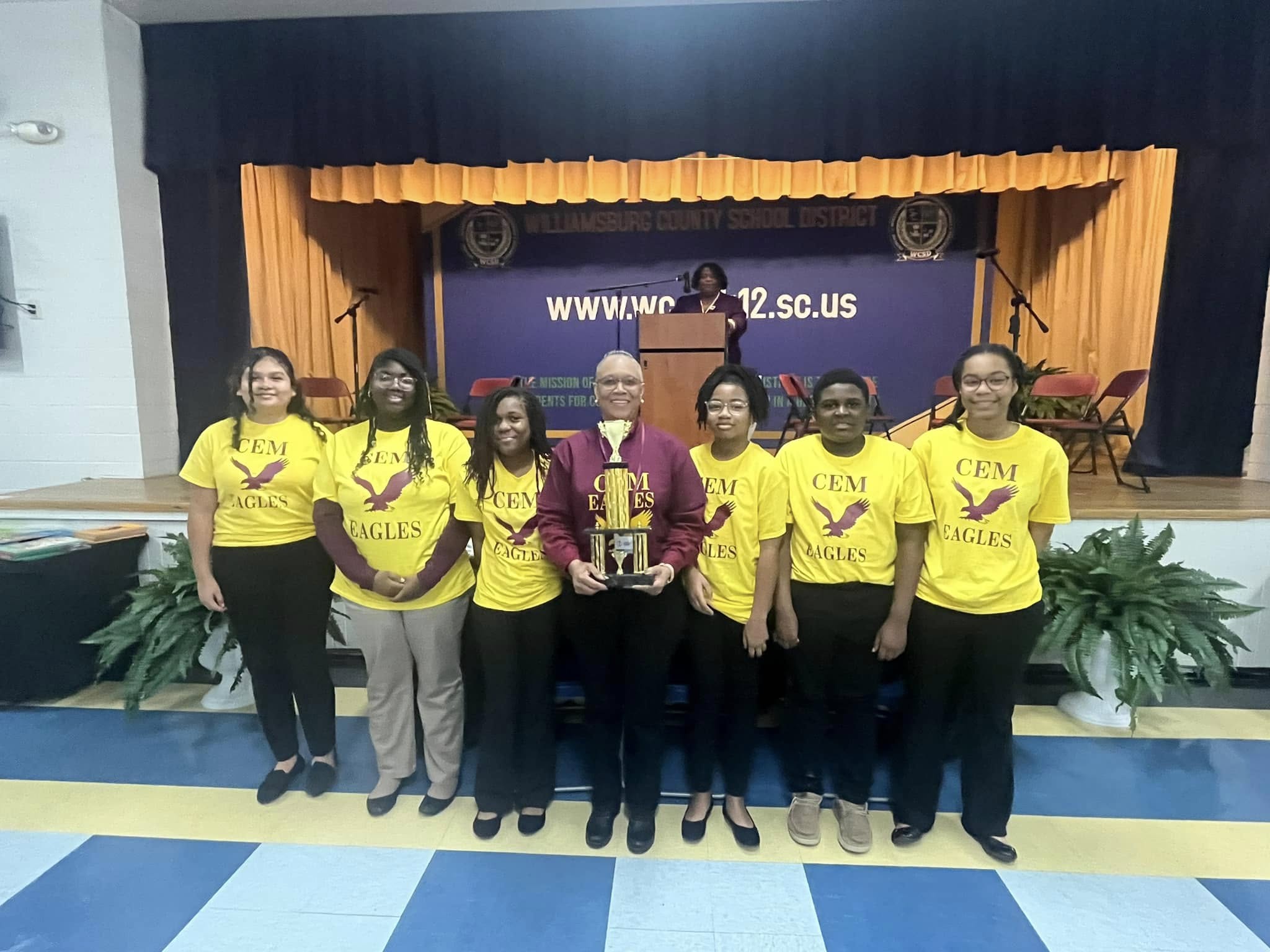 lady standing in the middle of six students holding trophy 