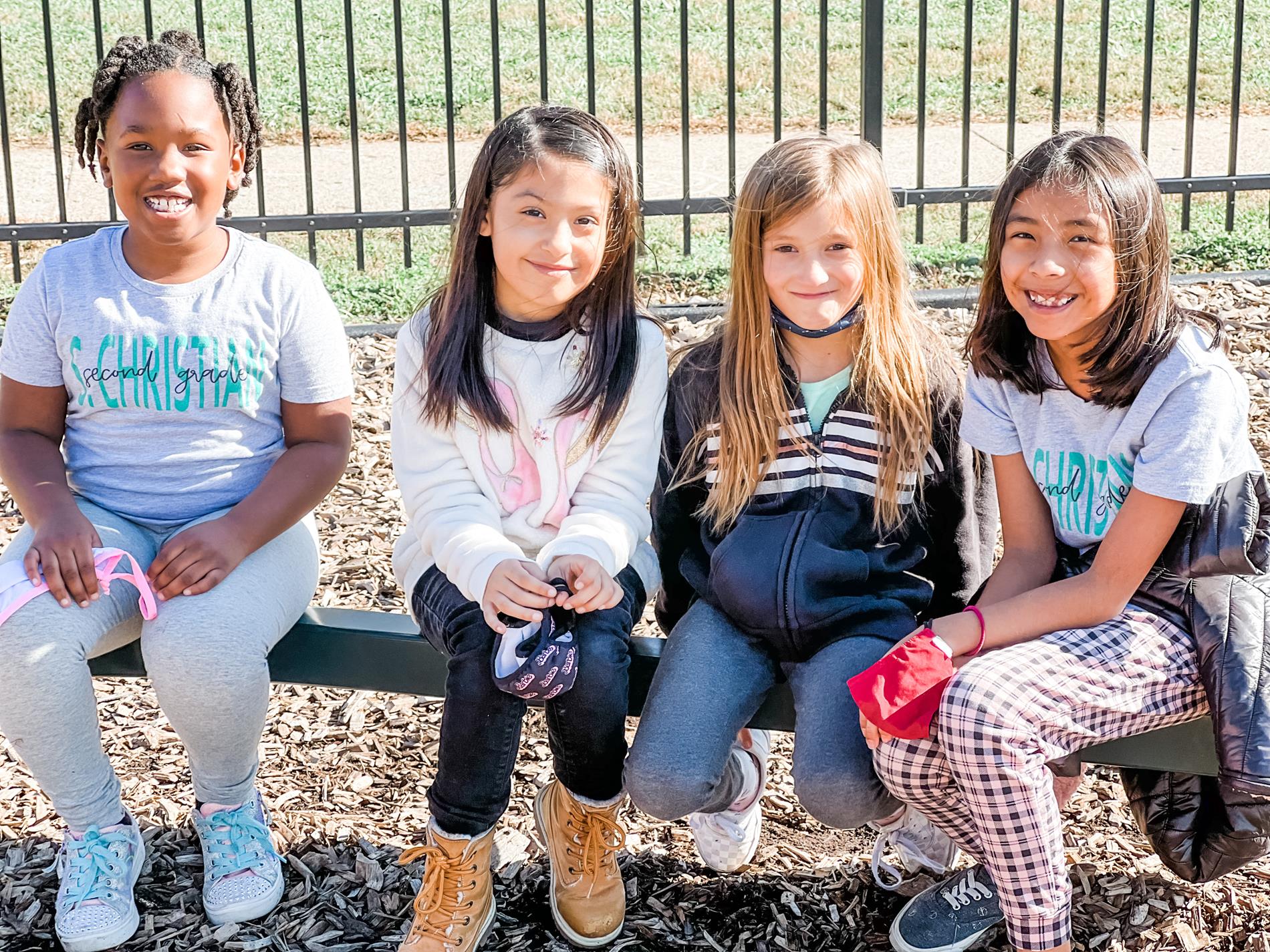4 2nd grade girls sitting and smiling on the play ground