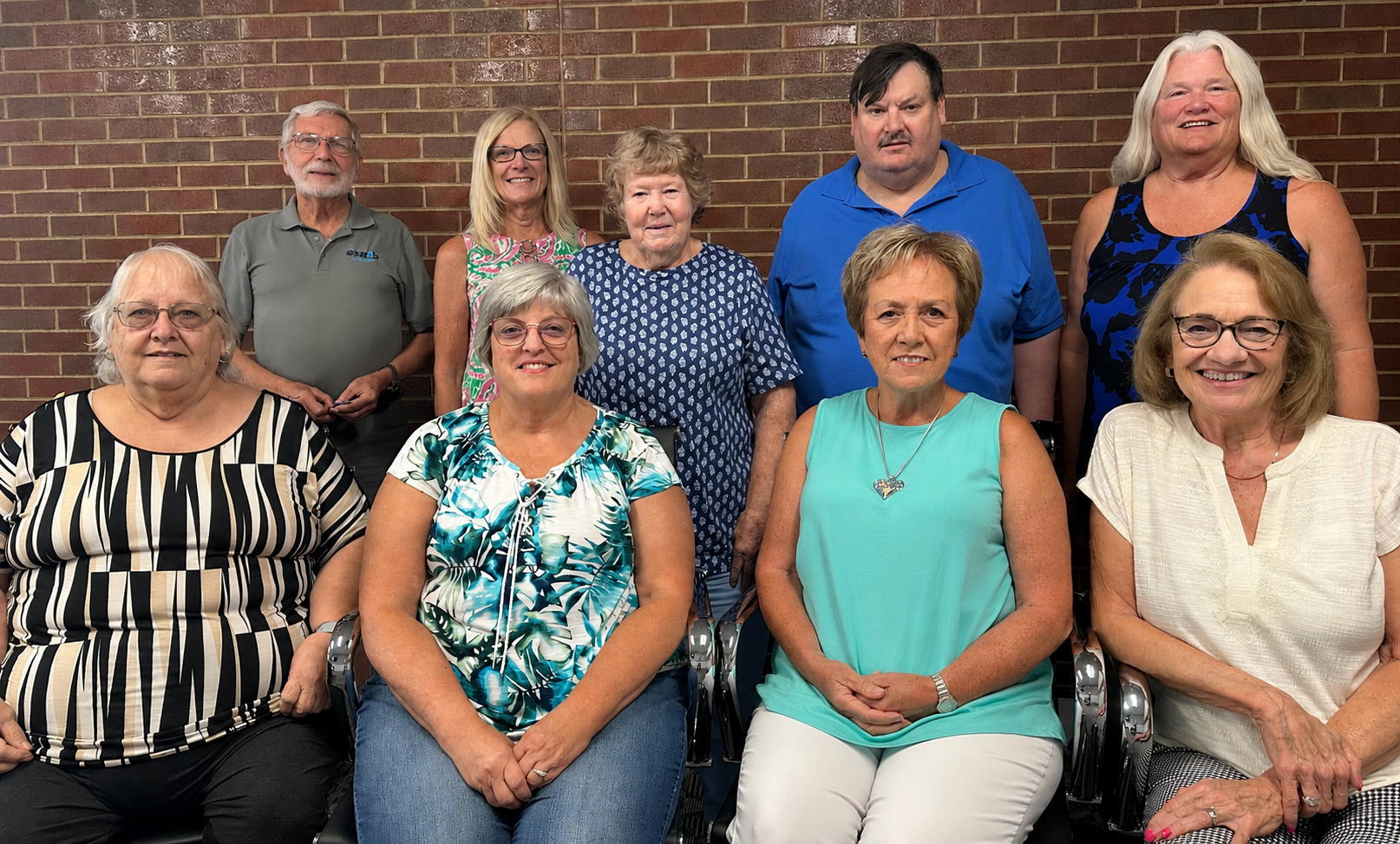 Nine ESU 4 Board members with a brick wall in the background. Four are seated in the front row and five are standing in the back row.