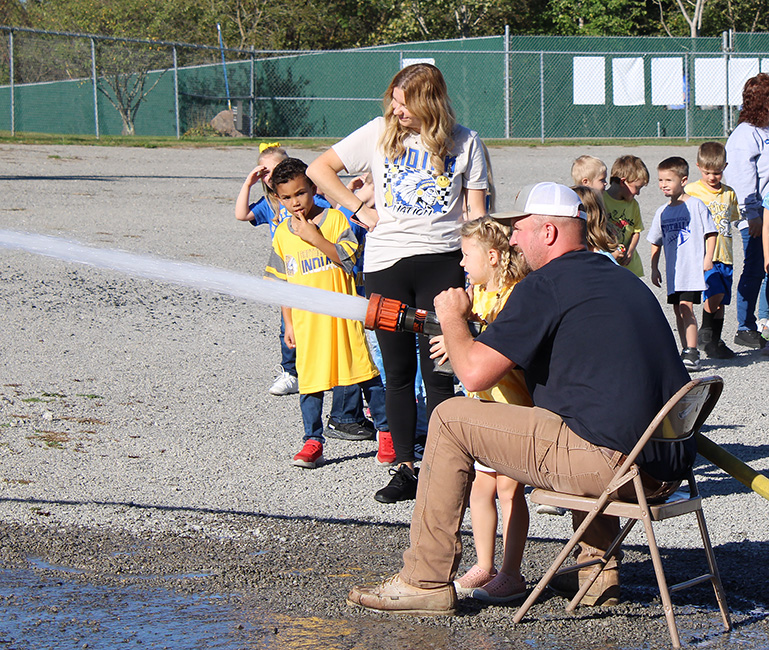 Fire Fighter Andrew Russell helps students with the fire hose