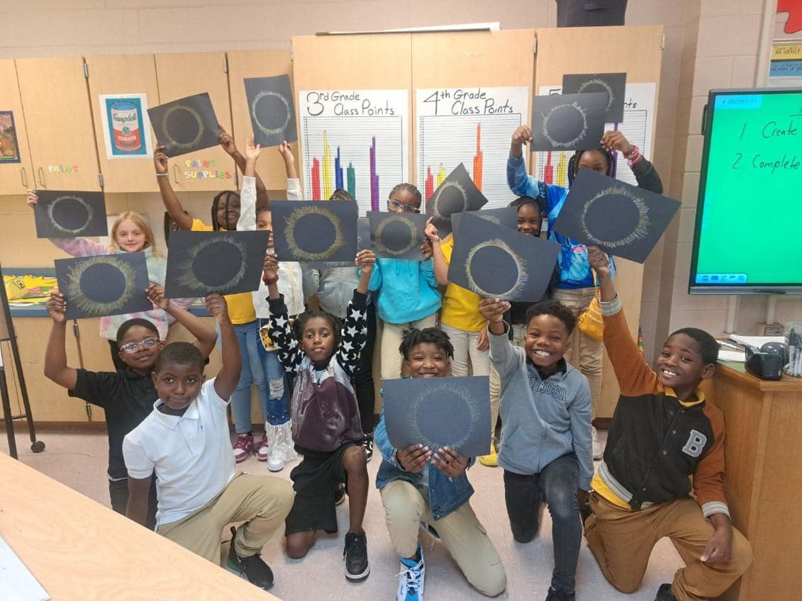 students holding up their art drawing of a solar eclipse 