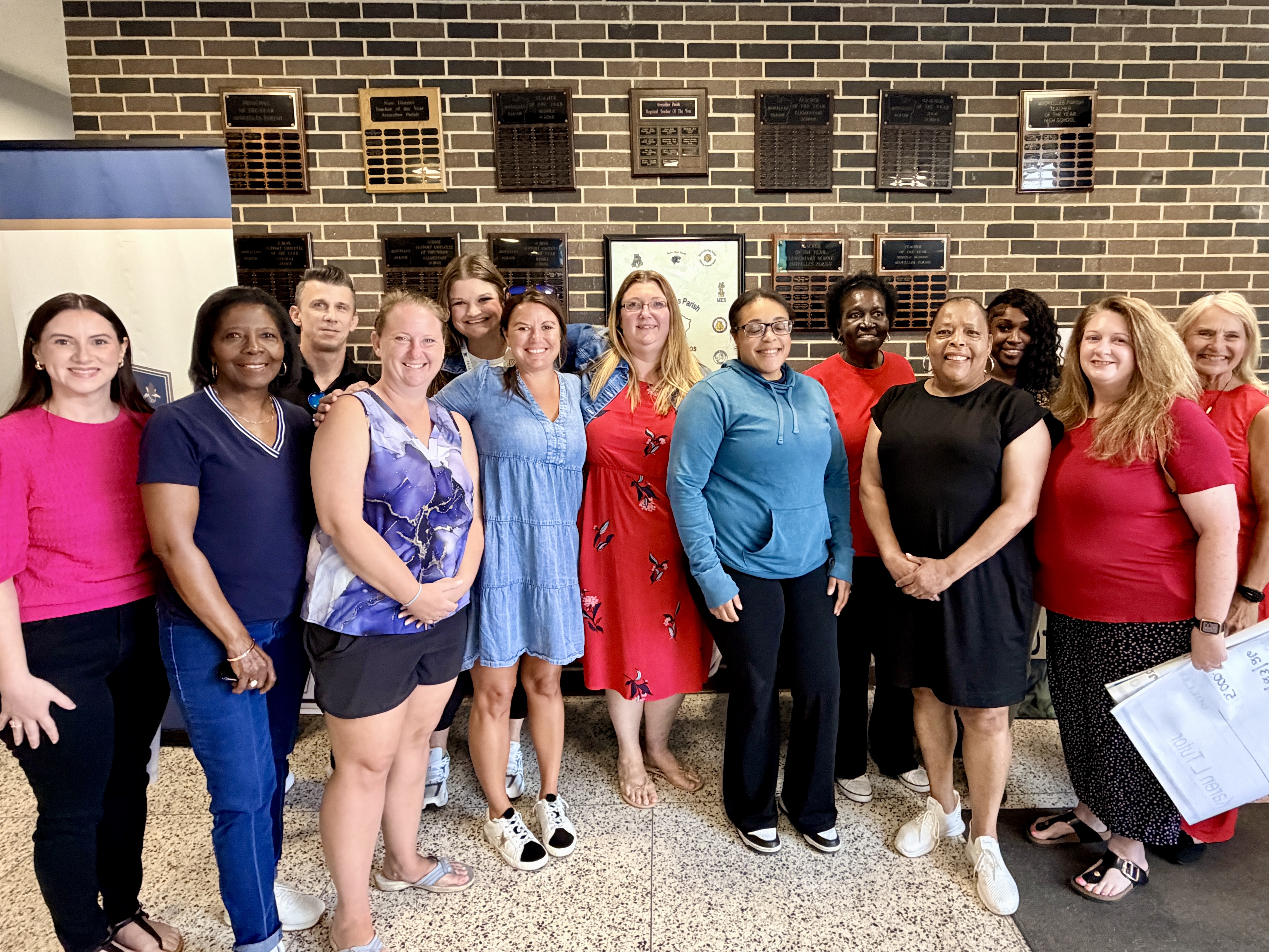 Group photo of Avoyelles Parish Schools educators recognized for exceptional student growth during the 2025-2026 school year. The teachers, representing schools across the district, stand together with Superintendent Karen Tutor after receiving $5,000 incentives for increasing student mastery by at least 5 percent. The group poses in front of a wall displaying school achievement plaques inside the district office.