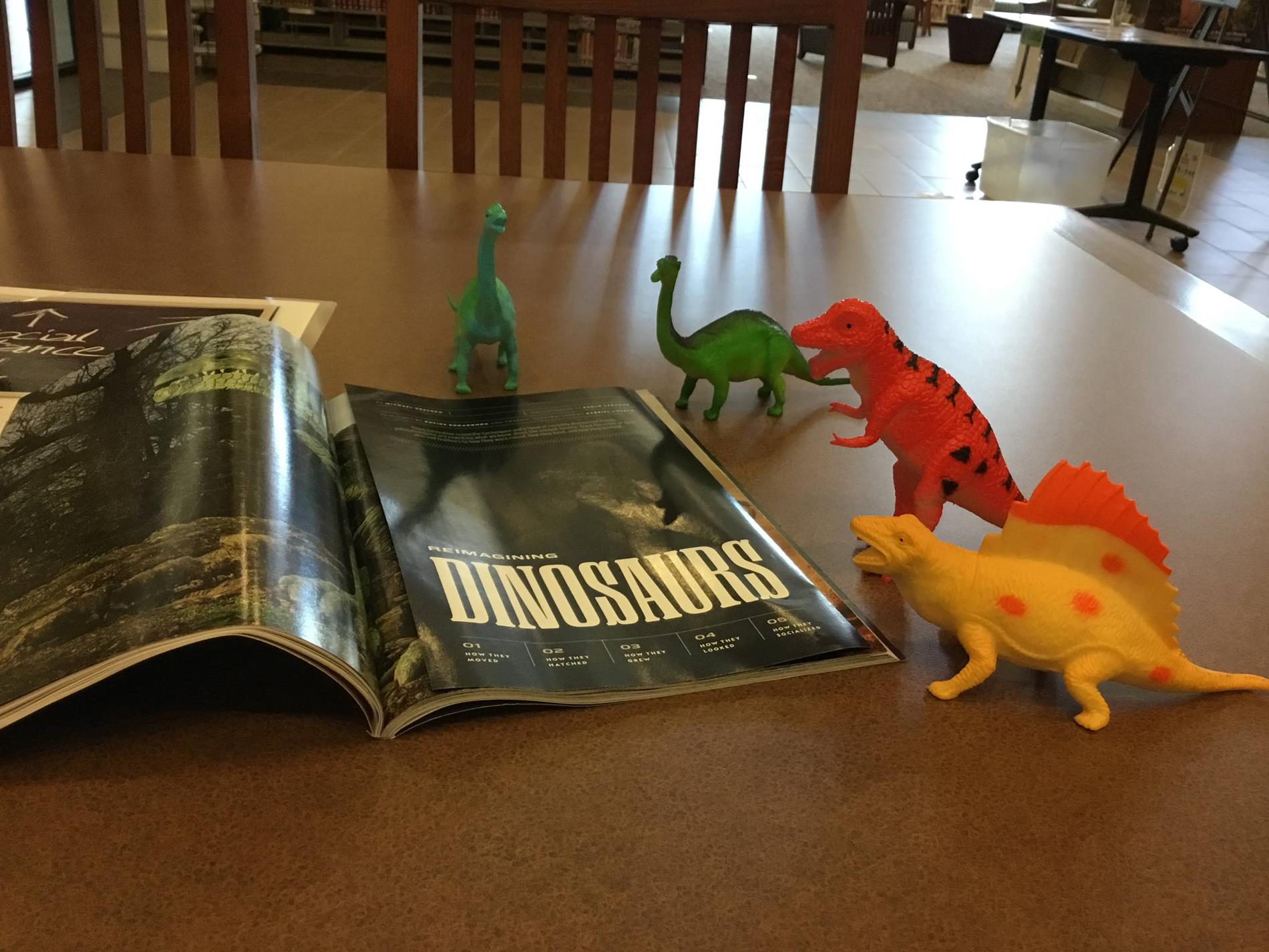 toy dinosaur figures arranged around a National Geographic Magazine opened to an article about Dinosaurs