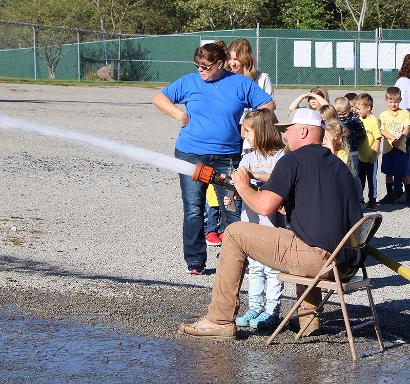 Fire Fighter Andrew Russell helps students with the fire hose