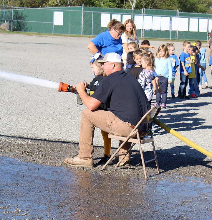 Fire Fighter Andrew Russell helps students with the fire hose