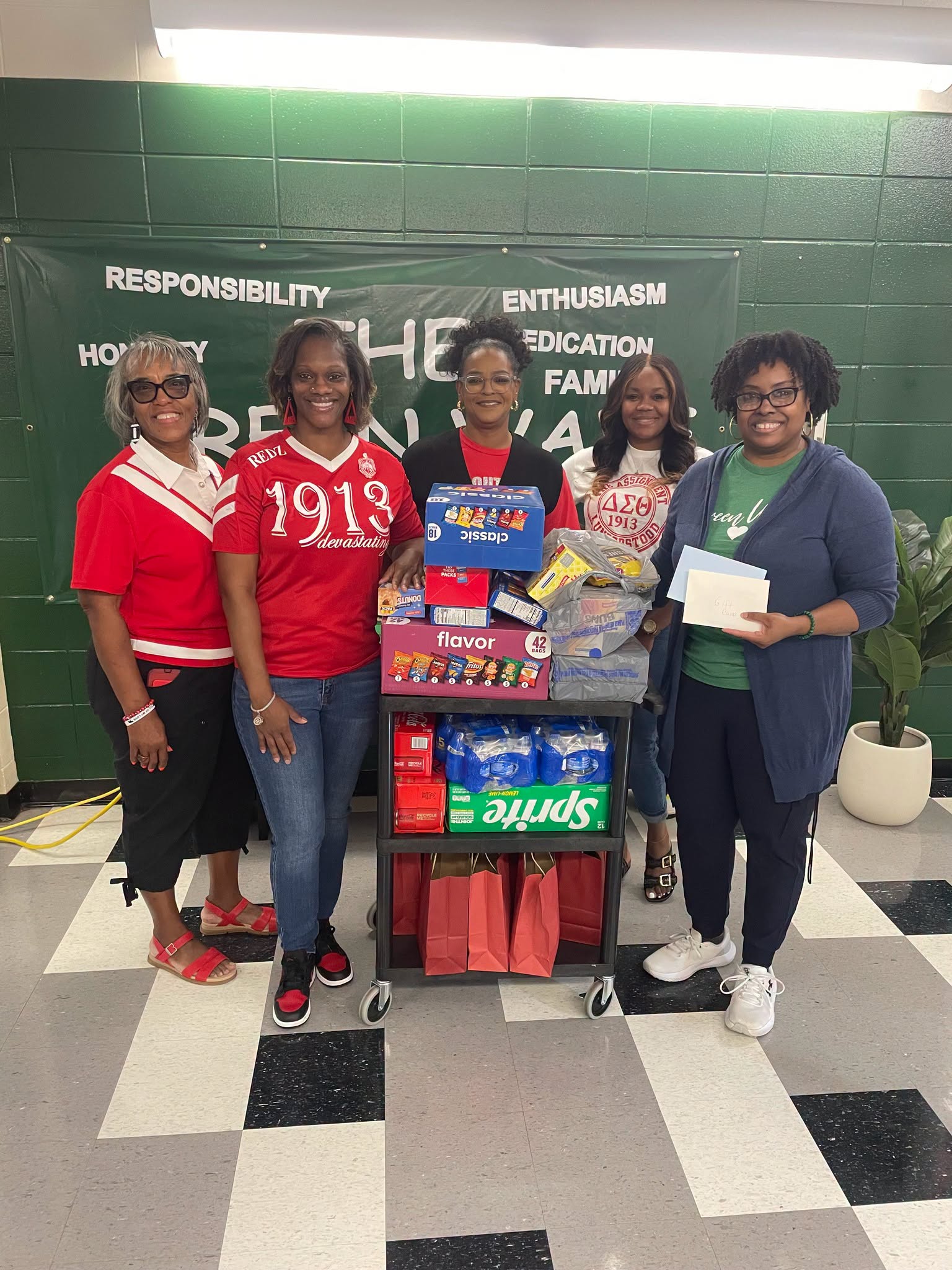 Members of Delta Sigma Theta Sorority, Inc. stand with WPHS–North Campus staff beside a cart filled with donated snacks, drinks, and other items for teachers, students, and school events.