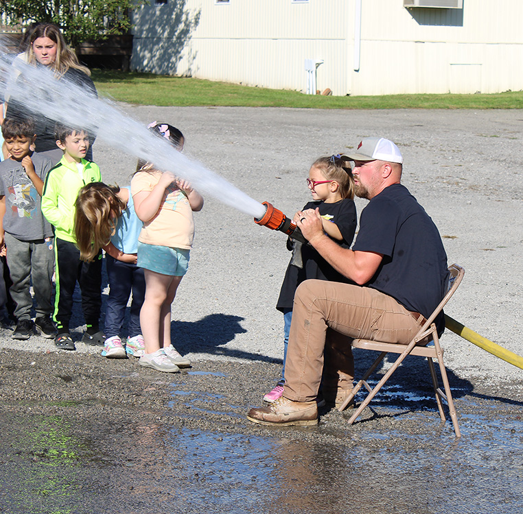 Fire Fighter Andrew Russell helps students with the fire hose