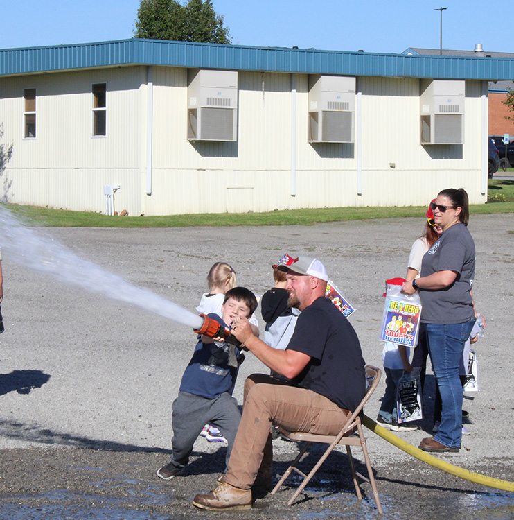 Fire Fighter Andrew Russell helps students with the fire hose