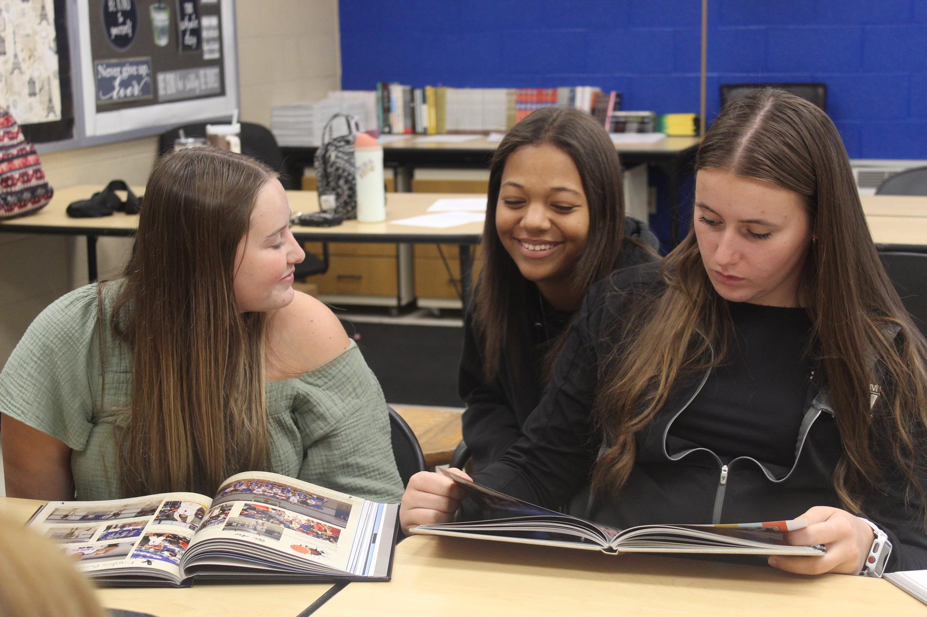 three girls laughing and smiling while looking at a yearbook