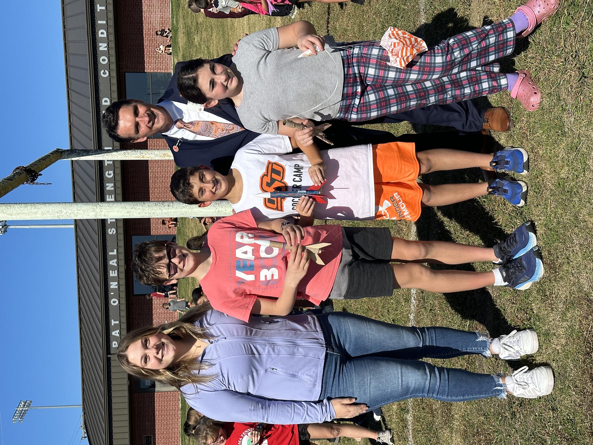 Sixth grade students hold rocket projects, posing with a teacher and ECU president. 