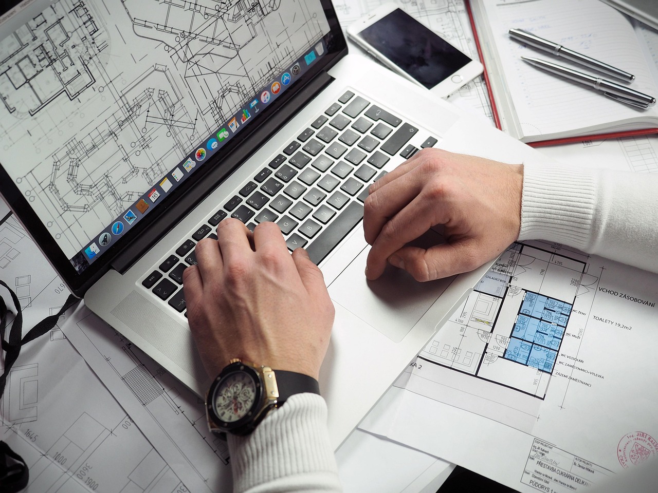 A man's hands work on a blueprint document on a laptop computer