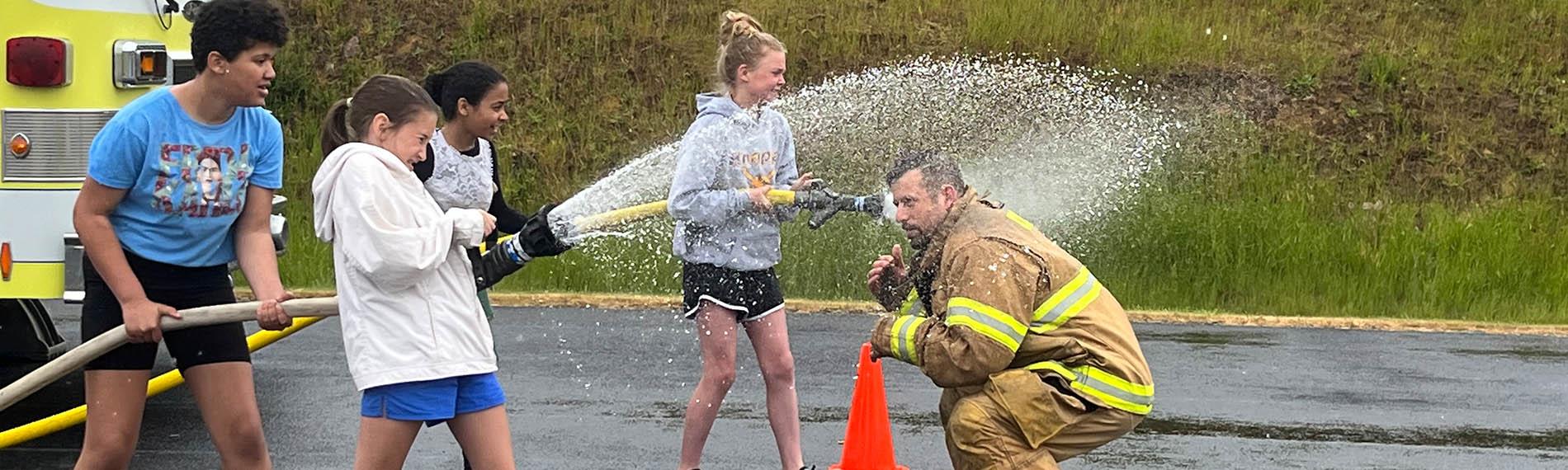 Students use a firehose as directed by a fireman during the HLE Field Day
