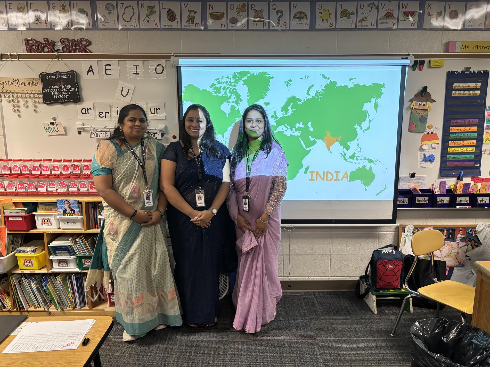 A group of paraprofessionals in sarees pose in front of a classroom