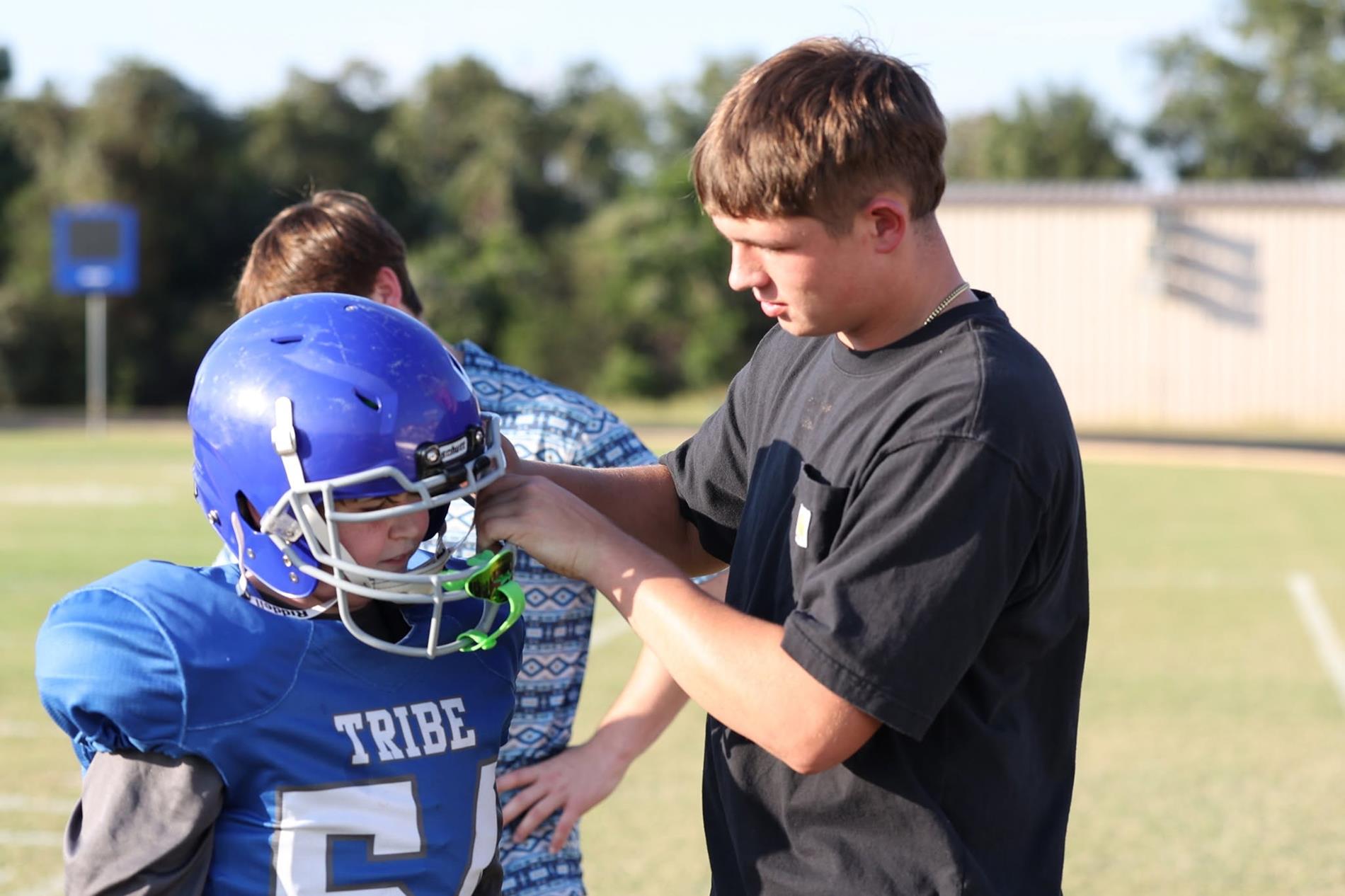 High school student assisting middle school student with football helmet